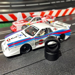 May include: A white, blue, and red race car with "Martini & Rossi" and "MiniAuto" printed on the side. The car is on a black track with a white line. There are two black tires on the track.