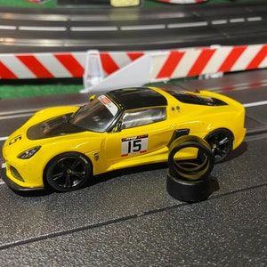 Può includere: Un'auto giocattolo gialla con dettagli neri e il numero 15 sul lato. L'auto è su una pista nera con linee bianche. Ci sono tre pneumatici neri accanto all'auto.