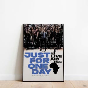 May include: A framed poster for "Just For One Day: The Live Aid Musical." The poster shows a man on stage with a crowd behind him. The title is in large blue letters, with the musical's name and an African continent silhouette.