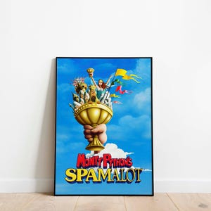 Peut inclure: Affiche encadrée du film Monty Python's Spamalot. L'image présente un calice doré tenu par une main, avec des personnages et des drapeaux sur fond de ciel bleu. Le titre "Monty Python's Spamalot" est affiché en rouge et jaune.