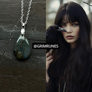 May include: A silver chain necklace with a teardrop-shaped pendant. The pendant is a dark, iridescent stone with shades of blue, green, and grey. The image also features a woman with long black hair and a raven. The text "@GRIMRUNES" is visible.