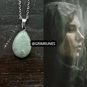 May include: A silver chain necklace with a teardrop-shaped, pale green pendant. The pendant has a speckled appearance. The image also features a woman with a dark veil. The text "@GRIMRUNES" is visible.