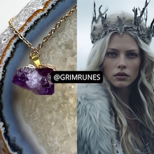 Pode incluir: Um colar de corrente de ouro com um grande pingente de ametista bruta. O pingente é de cor roxo escuro e tem uma forma natural irregular. O colar é apresentado em um fundo branco e cinza.