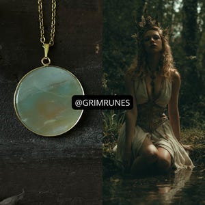 Pode incluir: Um colar dourado com um pingente grande e redondo com uma pedra azul clara e castanha. O colar é exibido em uma superfície escura. A imagem inclui o texto "@GRIMRUNES".