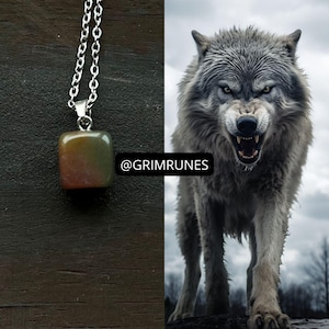 Pode incluir: Colar com corrente prateada e pingente quadrado com tons de verde, castanho e vermelho. A imagem também mostra um lobo rosnando com pelo cinzento contra um céu nublado. O texto "@GRIMRUNES" é visível.