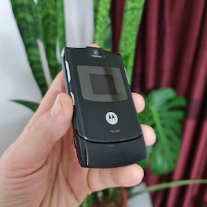 May include: A black flip phone with a silver trim and a Motorola logo. The phone is closed and has a small screen on the front.