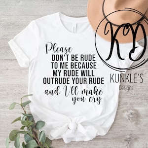 以下が含まれることがあります： 白いTシャツに黒い文字で「Please don't be rude to me because my rude will outrude your rude and I'll make you cry」と書かれています。文字は筆記体です。Tシャツは木製の表面に置かれ、茶色の帽子と「KD KUNKLE'S Designs」というロゴがあります。