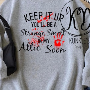 Könnte beinhalten: Grauer Pullover mit einer schwarzen Grafik, auf der "Keep it up you'll be a strange smell in my attic soon" steht. Die Grafik hat rote Blutspritzer und einen roten Handabdruck. Der Text "KUNKLE'S Designs" befindet sich ebenfalls auf dem Pullover.