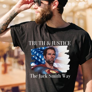 May include: A black t-shirt with a graphic of a man in a Superman costume with an American flag behind him. The text "Truth & Justice The Jack Smith Way" is printed on the shirt.