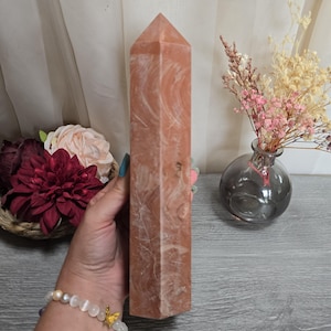 May include: A tall, hexagonal crystal tower with a polished, smooth surface in shades of peach and terracotta, featuring intricate white swirling patterns throughout the stone. The object has a pointed, faceted top and a flat base.