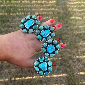 May include: Four silver rings featuring clusters of turquoise stones in various shapes and sizes. Each ring is marked with a red number from one to four, showcasing a central turquoise stone surrounded by smaller turquoise cabochons in metal settings.
