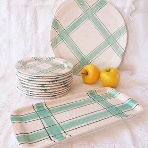 Peut inclure: Un ensemble de plats en céramique vintage et un plateau de service avec un motif à carreaux vert et blanc. Les assiettes sont empilées et le plateau est posé à plat. Il y a deux pommes vertes en arrière-plan.