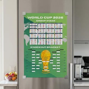 Op de afbeelding: Een groen en wit World Cup 2026 Group Stage en Knockout Bracket poster wordt weergegeven op een roestvrijstalen koelkast. De poster toont een wereldkaart, wedstrijdschema's en een gouden trofee-illustratie.