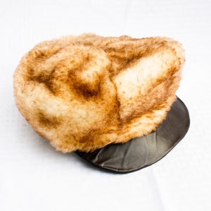 Puede incluir: Un sombrero de piel sintética marrón y blanco con una visera de cuero marrón.