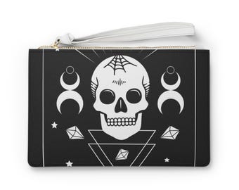 May include: Black clutch with a white skull design, spiderweb, crescent moons, diamonds, and stars. The clutch has a white wrist strap and a gold zipper. The design is a gothic or occult theme.