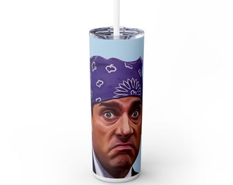 Puede incluir: Un vaso blanco con un fondo azul que presenta un retrato de un hombre con una bandana morada. El vaso tiene una pajita blanca y una tapa plateada. La cara del hombre está pintada con una expresión seria.