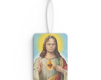 May include: Rectangular air freshener featuring a portrait of a man with long brown hair, glasses, and a serious expression, styled in the manner of religious iconography. The background is a yellow halo against a blue sky. The air freshener has a white string for hanging.