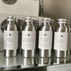 May include: A set of eight silver metal reed diffuser bottles with white labels. The labels feature the brand name "Absolute Melter" and different scents, including "Myrrh & Tonka", "Rock Salt & Driftwood", "Velvet Rose & Oud", and "La Vie Est Belle".