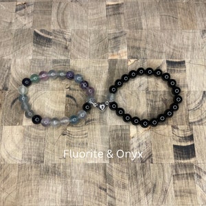 Peut inclure: Deux bracelets en perles reli&eacute;s par un charm en forme de c&oelig;ur argent&eacute;. Le bracelet de gauche est compos&eacute; de perles de fluorite multicolores. Le bracelet de droite est compos&eacute; de perles d'onyx noir. Fluorite & Onyx.