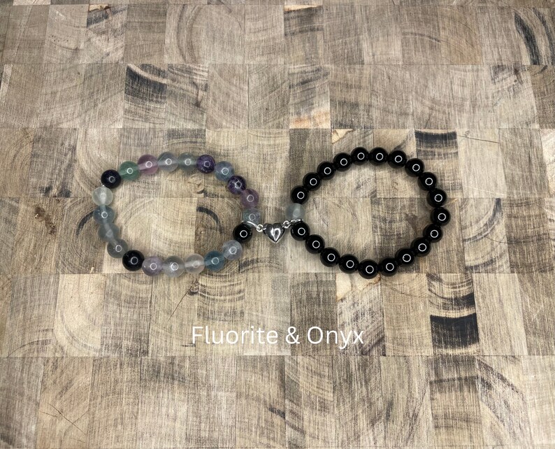 Peut inclure: Deux bracelets en perles reli&eacute;s par un charm en forme de c&oelig;ur argent&eacute;. Le bracelet de gauche est compos&eacute; de perles de fluorite multicolores. Le bracelet de droite est compos&eacute; de perles d'onyx noir. Fluorite & Onyx.
