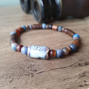 May include: A beaded bracelet featuring brown wooden beads, blue and grey agate beads, and a white ceramic bead with blue and grey marbling.