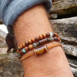 Peut inclure: Un ensemble de trois bracelets avec des perles en bois brun, un cordon en cuir brun et une perle en œil de tigre.