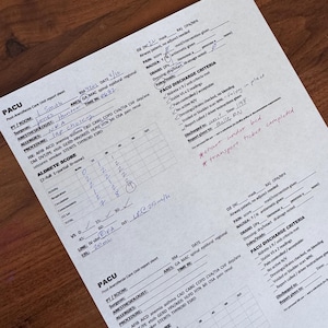 May include: A white Post-Anesthesia Care Unit report sheet with black printed text and handwritten blue and red ink entries. The document includes patient information, an Aldrete score table, and discharge criteria with checkmarks and notes.