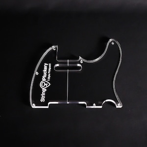 Könnte beinhalten: Ein transparentes T-Style Gitarren-Schlagbrett aus Acryl mit dem weiß aufgedruckten Text String Pluckery und T-Style Pickguard sowie einem Logo. Das Schlagbrett enthält vorgebohrte Löcher für Schrauben und einen Ausschnitt für den Tonabnehmer.