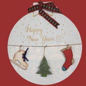May include: A round, light blue Christmas ornament with the words "Happy New Year!!!" in gold script. It features a plaid ribbon, a wooden ice skate, a green tree, and a red stocking hanging from a string. The background has a winter village scene.