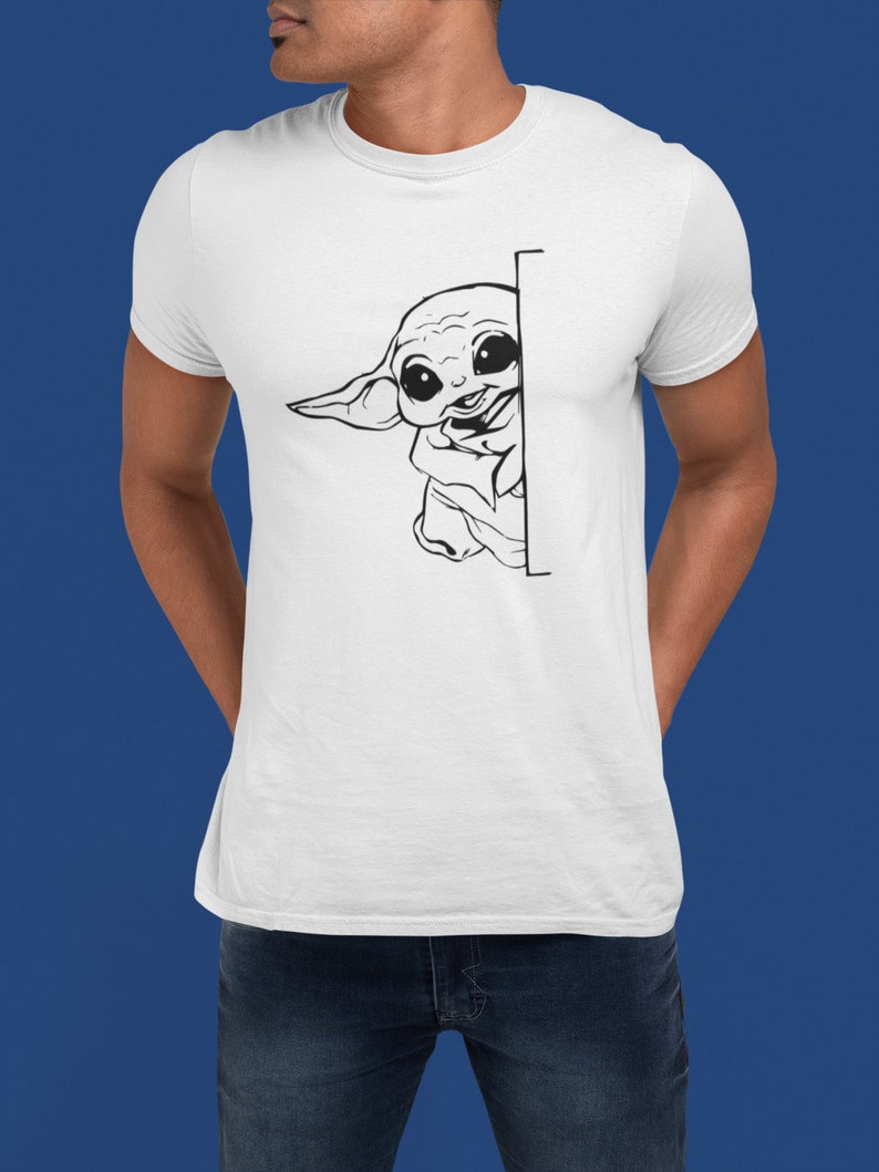 May include: A white t-shirt with a black and white illustration of a cartoon character peeking around a corner. The character has large eyes and a small mouth.