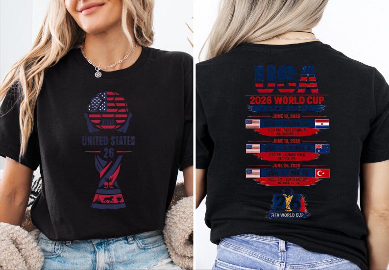 May include: Black t-shirt with a graphic design for the 2026 World Cup, featuring the USA flag and the text "UNITED STATES 26". The back of the shirt lists game dates and locations.