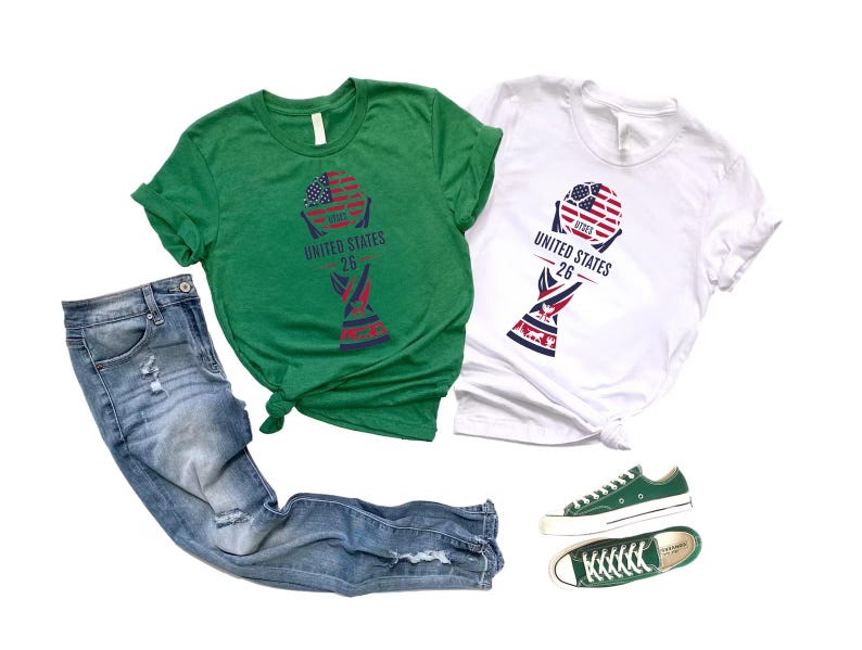 May include: Two t-shirts, one green and one white, with a graphic design featuring a soccer ball with an American flag design and the text "UNITED STATES 26". The image also includes a pair of blue jeans and green sneakers.