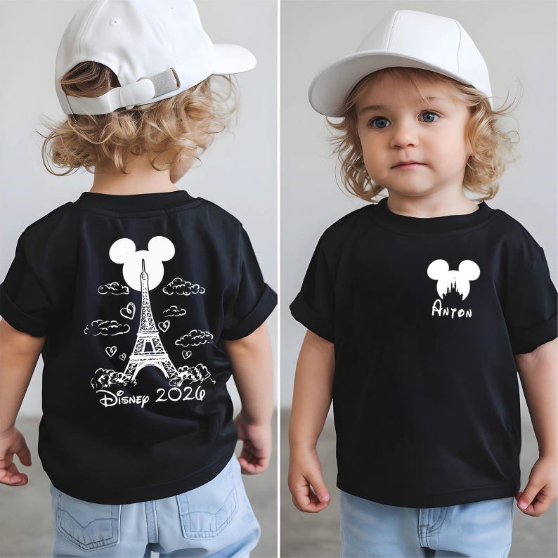 May include: Black t-shirt with a white Mickey Mouse silhouette and the name "Anton" printed below it. The back of the shirt features a design of the Eiffel Tower, clouds, hearts, and the text "Disney 2020". The child is wearing a white baseball cap.