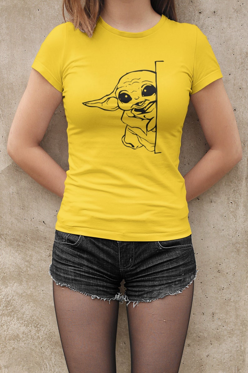 May include: A yellow t-shirt with a black and white graphic of a cartoon character peeking from behind a wall. The character has large eyes and a wide mouth.