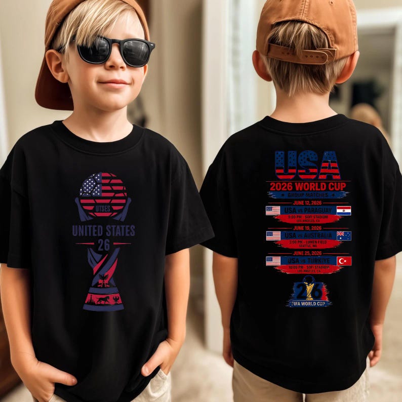 May include: Black t-shirt with a soccer ball graphic featuring the American flag and the text "UNITED STATES 26". The back of the shirt displays "USA 2026 WORLD CUP" and match details.
