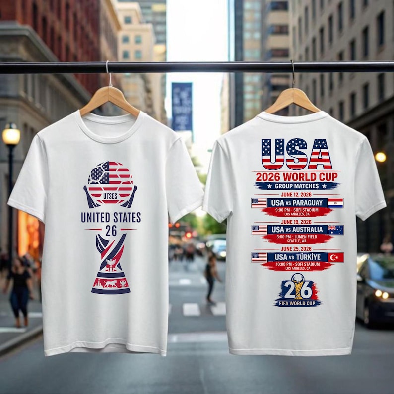 May include: White t-shirts with a soccer-themed design. One shirt features a soccer ball graphic with the text "UNITED STATES 26". The other shirt displays "USA 2026 WORLD CUP" with match details, including dates, opponents, and locations.
