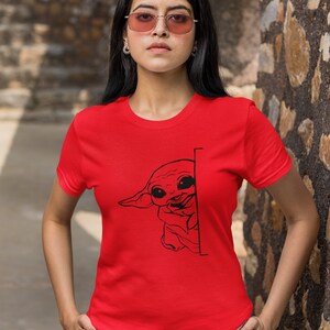 May include: A red t-shirt with a black graphic of a cartoon character peeking around a corner. The character has large eyes and a small mouth.