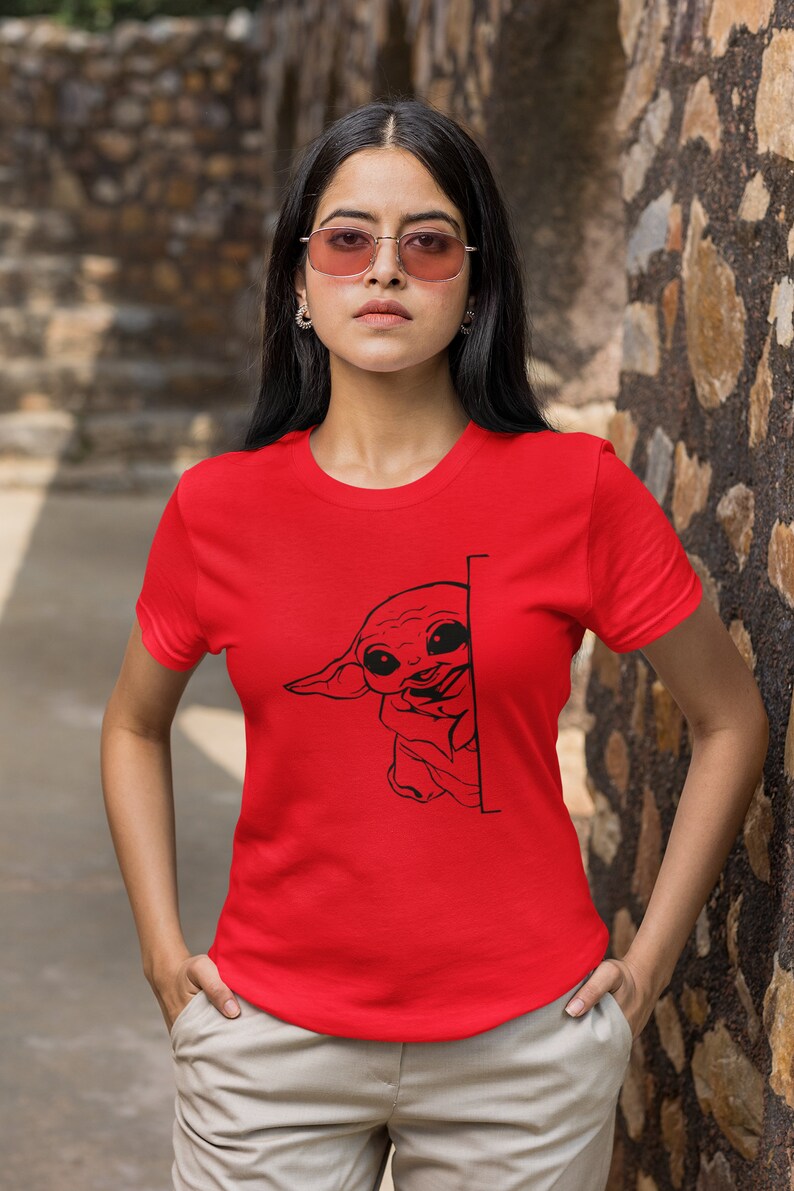 May include: A red t-shirt with a black graphic of a cartoon character peeking around a corner. The character has large eyes and a small mouth.