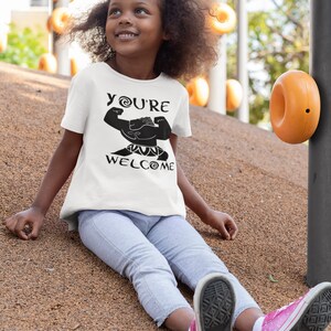 May include: A white t-shirt with a black graphic of a cartoon character with the text "YOU'RE WELCOME" on it. The character is flexing its muscles.