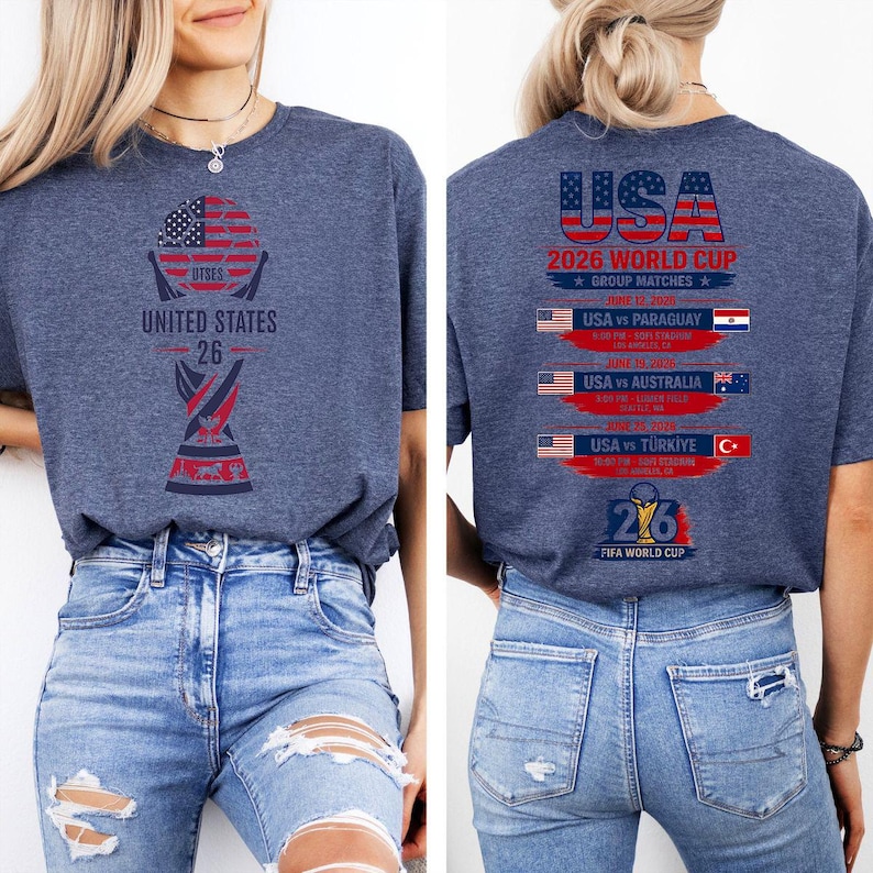 May include: A navy blue t-shirt with a graphic design for the 2026 FIFA World Cup. The front features a trophy design with the text "UNITED STATES 26". The back displays "USA 2026 WORLD CUP" and match details.