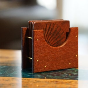 May include: A set of wooden coasters with a seashell design, stacked in a wooden holder. The holder has a dark brown finish and brass accents.
