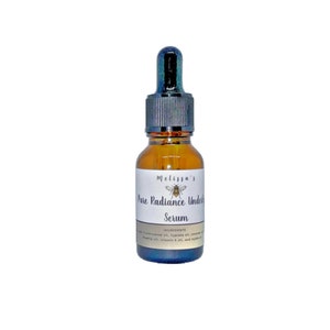 K&ouml;nnte beinhalten: Eine kleine bernsteinfarbene Glasflasche mit einem schwarzen Tropfer. Die Flasche ist mit "Melissa's Pure Radiance Under Eye Serum" und einer kleinen Bienenillustration beschriftet. Das Etikett listet auch "Zutaten:  Frankincense&ouml;l, Zypressen&ouml;l, Lavendel&ouml;l, Avocado&ouml;l, Vitamin E &Ouml;l und Jojoba&ouml;l" auf.