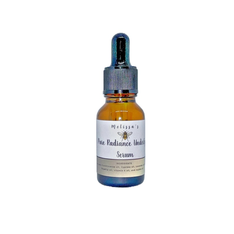 K&ouml;nnte beinhalten: Eine kleine bernsteinfarbene Glasflasche mit einem schwarzen Tropfer. Die Flasche ist mit "Melissa's Pure Radiance Under Eye Serum" und einer kleinen Bienenillustration beschriftet. Das Etikett listet auch "Zutaten:  Frankincense&ouml;l, Zypressen&ouml;l, Lavendel&ouml;l, Avocado&ouml;l, Vitamin E &Ouml;l und Jojoba&ouml;l" auf.
