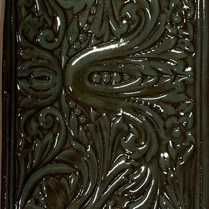 May include: A ceramic tile with a raised, intricate design of swirling leaves and flowers in shades of green and brown.
