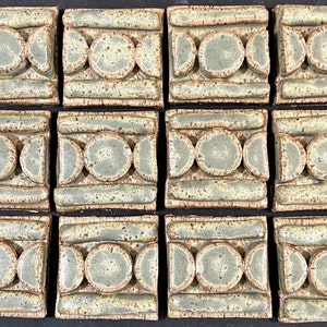 May include: Twelve square ceramic tiles with a repeating pattern of circles and crescent moons. The tiles are a light green color with brown accents.