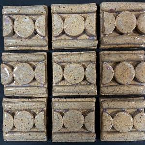 May include: Nine square ceramic tiles with a speckled brown glaze. Each tile features a repeating pattern of three circles and three half-circles.