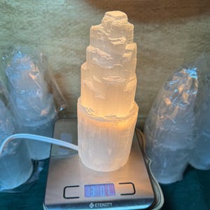 May include: A white selenite crystal lamp on a digital scale. The lamp is lit and has a warm glow. The scale reads 3.01.