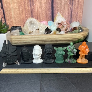 May include: A collection of Star Wars character figurines, including Darth Vader, a Stormtrooper, and Yoda. The figurines are various colors, including black, white, green, and orange. A wooden ruler is placed in front of the figurines.