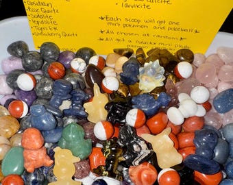 May include: A vibrant assortment of gemstones and small figurines, such as red jasper, dream amethyst, and blue aventurine. The image also includes small, round, red and white balls. A yellow note lists the gemstones and mentions mini Pokemon characters.