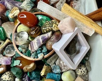 May include: A variety of polished and raw crystals and stones in a bowl, including amethyst, clear quartz, tiger's eye, and green aventurine. There are also several selenite wands and a pink rose quartz.